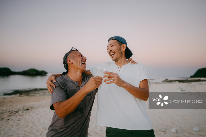 两个男人在黄昏时分的海滩上敬酒图片素材