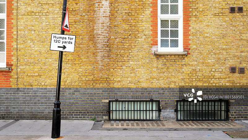 英国伦敦带窗户的黄灰色风化砖墙、人行道和带路标的柱子图片素材
