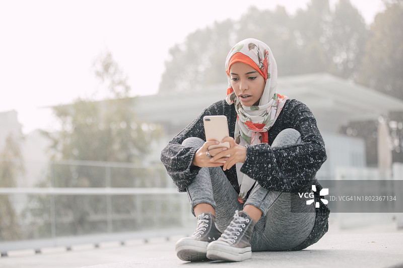 年轻学生坐在长椅上用手机发短信图片素材