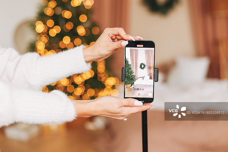 在圣诞节客厅里，身穿白色毛衣的年轻女子打开手机上的视频录制图片素材
