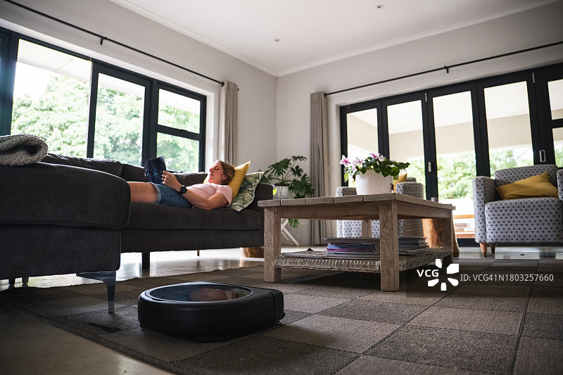 母亲读书时，机器人真空吸尘器正在清洁图片素材
