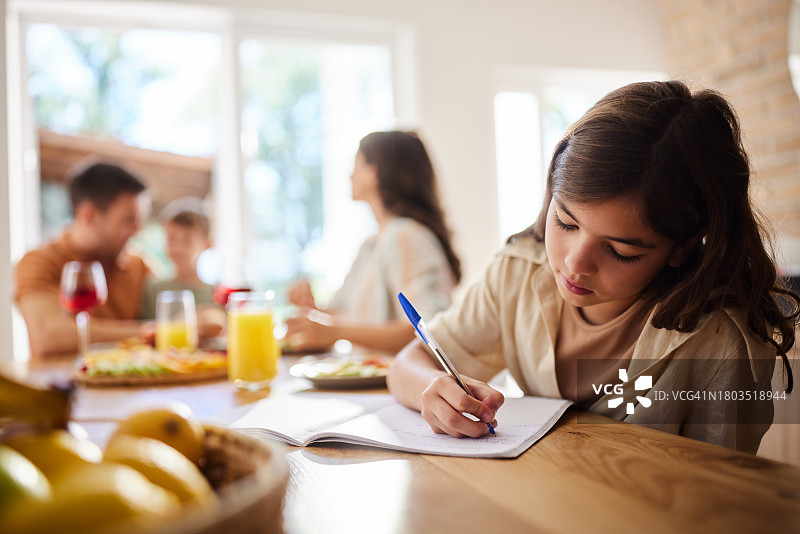 在餐桌上写作业的可爱小女孩。图片素材