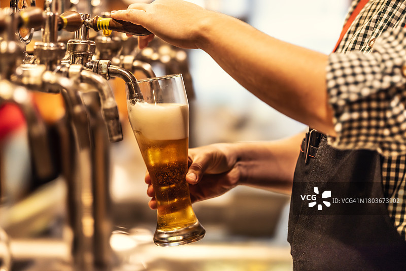 酒吧里，店主将泡沫淡啤酒倒入玻璃杯中图片素材