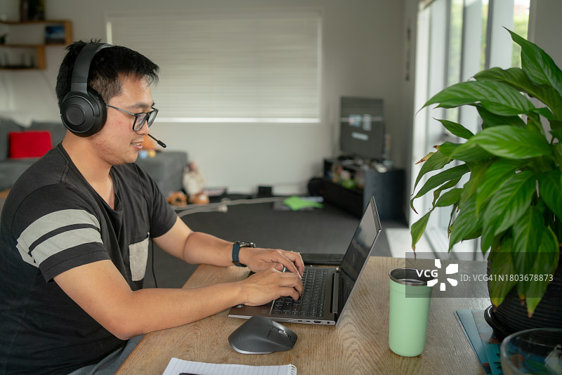 年轻的亚洲男人在家工作时在笔记本电脑上打字。图片素材