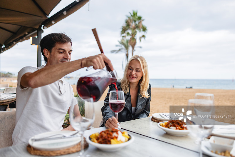 在海滩餐厅外，西班牙男人为女友的玻璃杯里倒桑格利亚汽酒图片素材