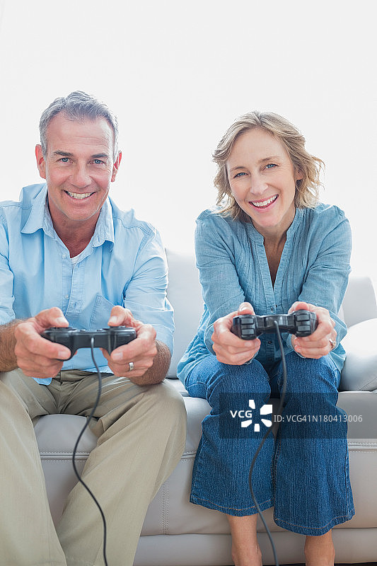 在沙发上一起玩电子游戏的微笑情侣图片素材