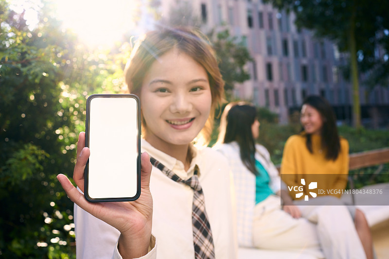 年轻的中国女人对着镜头展示空的手机屏幕，面带微笑图片素材