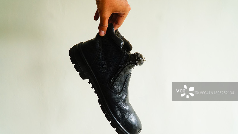 手拿黑色旧靴子，白色背景图片素材