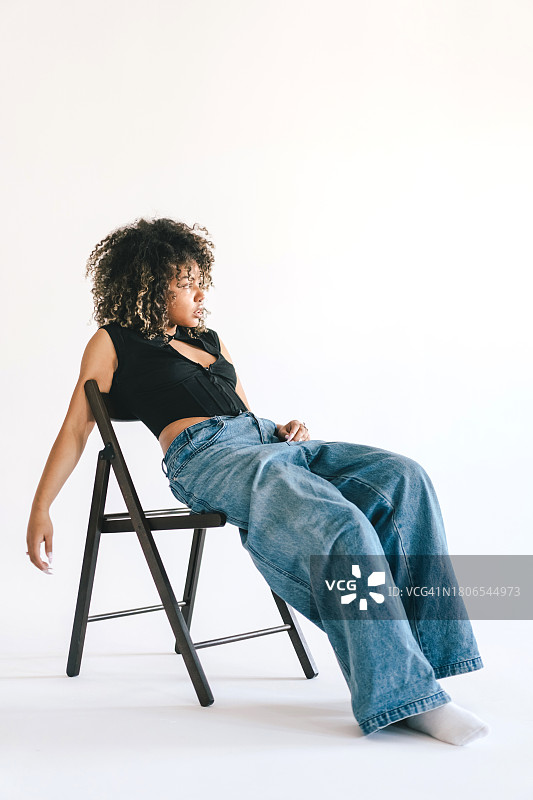 一位美丽的年轻女子在白色工作室的椅子上摆姿势图片素材