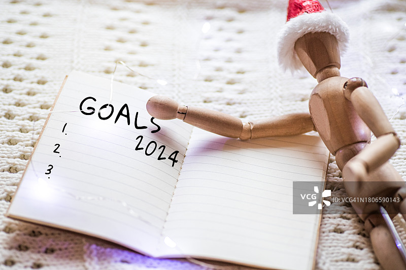 2024年目标，笔记本是新起点的象征，代表新的开始和改变的机会，在针织毯子上，戴着圣诞帽的木制小人图片素材