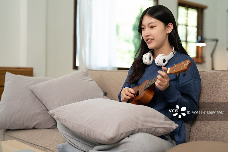 年轻女人在家享受弹奏尤克里里放松图片素材