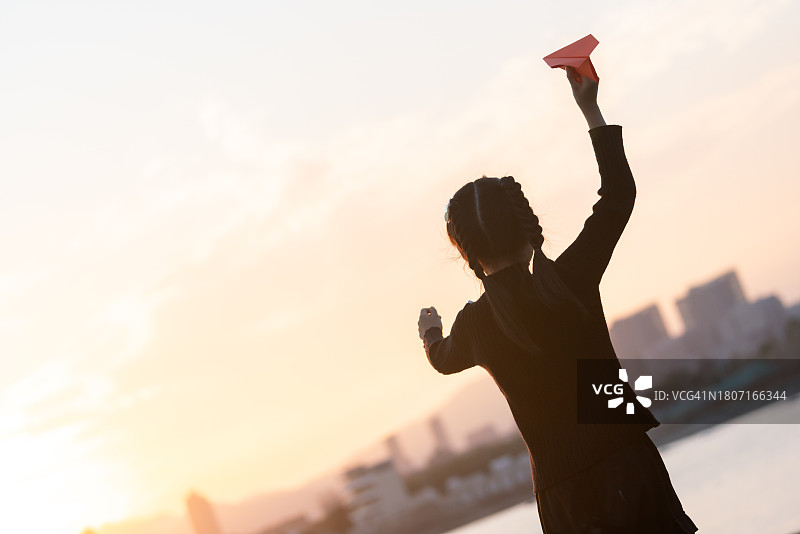 女孩在海边玩纸飞机，金色的阳光洒在海面上图片素材