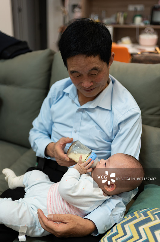 爷爷在沙发上给女婴喂奶图片素材