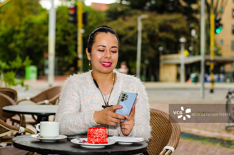 女子在咖啡店吃蛋糕，使用智能手机图片素材