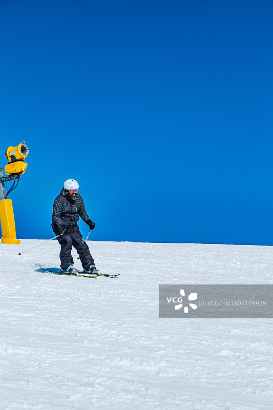 滑雪者身着滑雪服在晴朗的天空下走下雪坡，冬季滑雪季假期图片素材