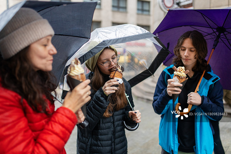 母亲和两个十几岁的孩子在布达佩斯市中心吃烟囱蛋糕图片素材