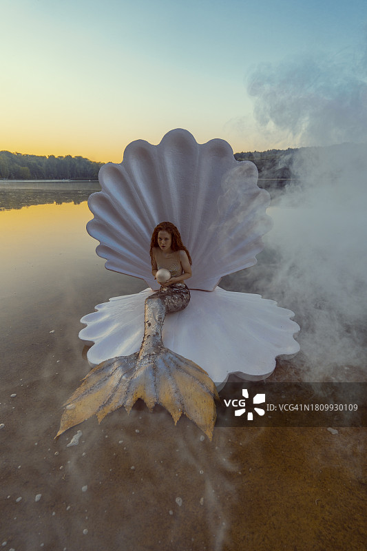 日落时分，海滩上拥有巨型贝壳的美丽红发美人鱼的抽象概念图片素材