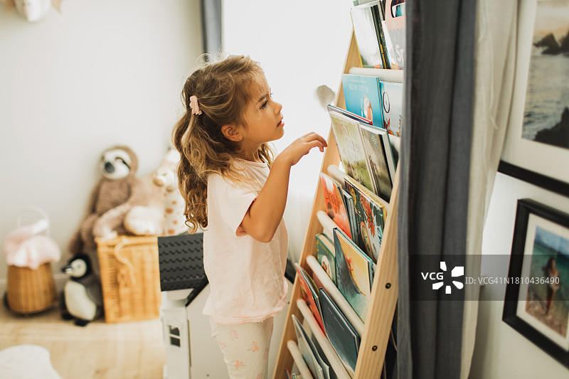 小女孩伸手去够书架上的书图片素材
