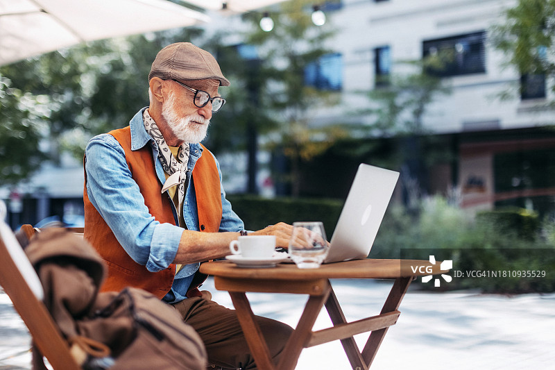 时尚老年男人在咖啡店使用笔记本电脑喝咖啡图片素材