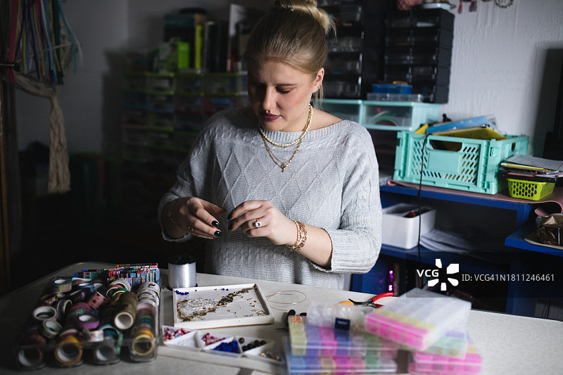 在家庭工作室里用珠子和线热情地创作最新杰作的金发美女艺术家图片素材