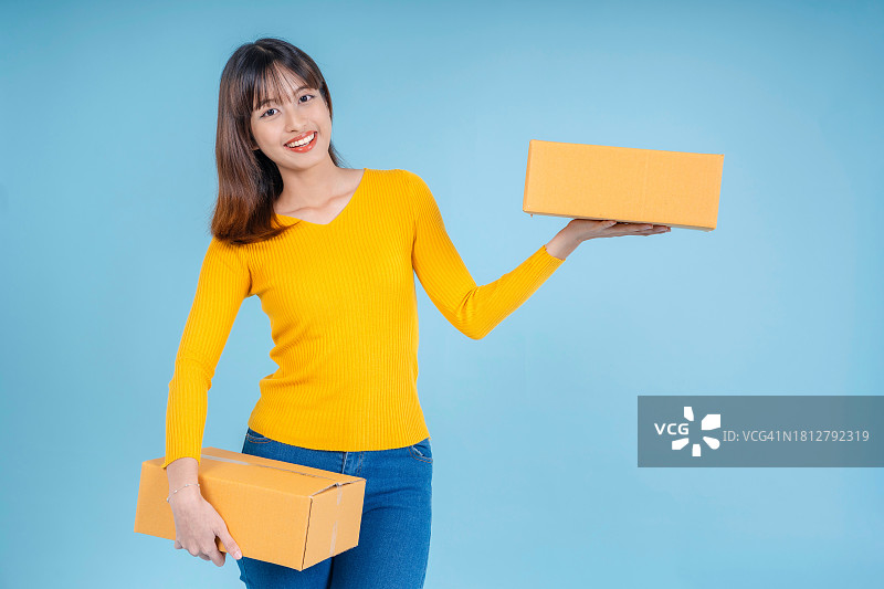 快乐的亚洲女人手拿包裹纸箱在白色背景下微笑。快递和运输服务概念。在线购物。在线销售图片素材