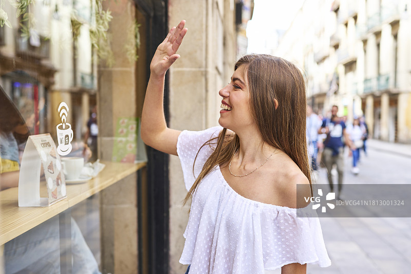 在咖啡店窗口挥手的漂亮白人女性图片素材