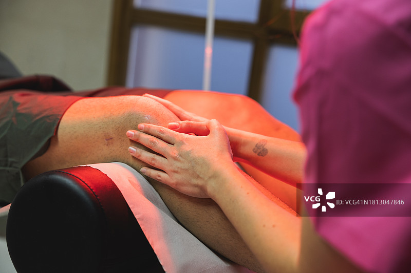 年轻理疗师在理疗中心用热灯对膝盖损伤进行治疗按摩图片素材
