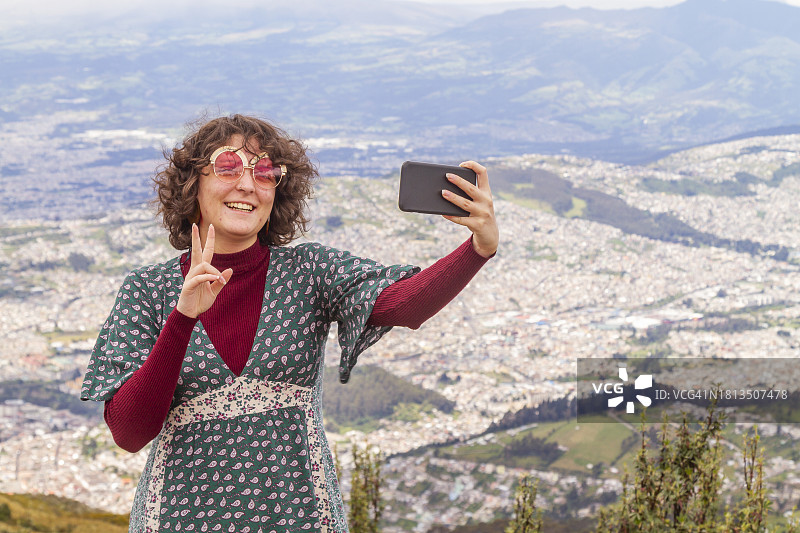 独自旅行的年轻少女在钦查火山顶用5G智能手机自拍。背景是厄瓜多尔首都：基多图片素材