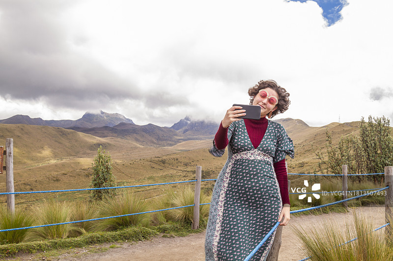 在皮钦查火山顶峰用5G智能手机自拍的年轻女性旅行者肖像，背景是厄瓜多尔首都基多图片素材