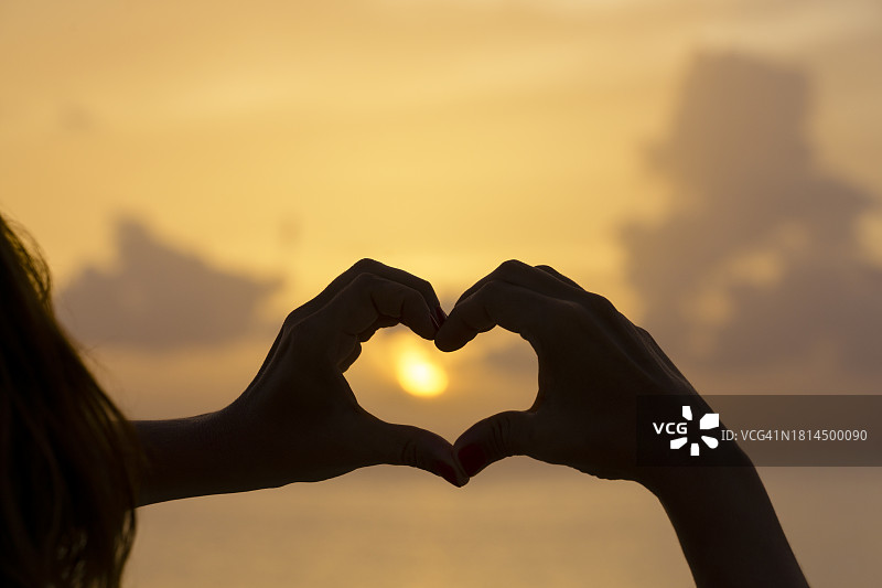 女人在日落时用手比心图片素材