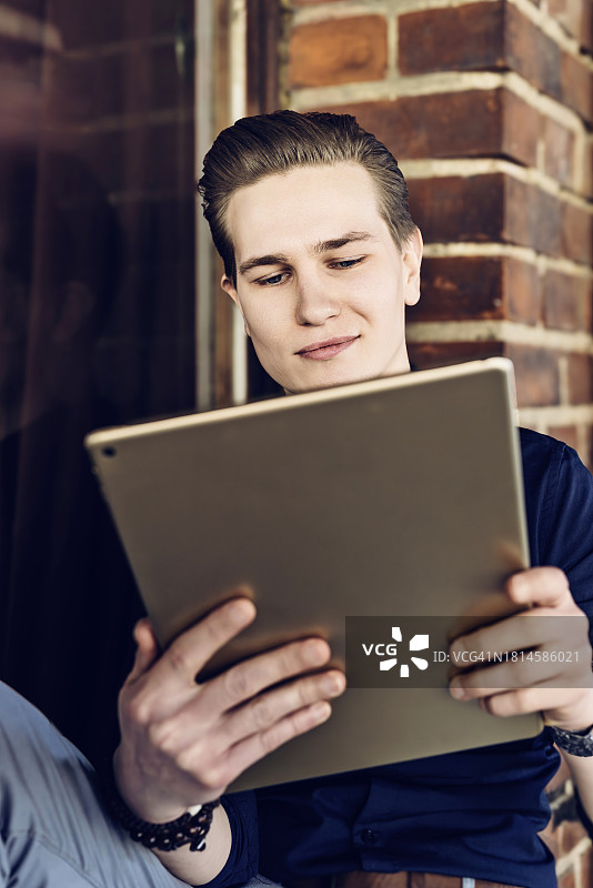 年轻商人坐在窗台上使用平板电脑放松身心图片素材