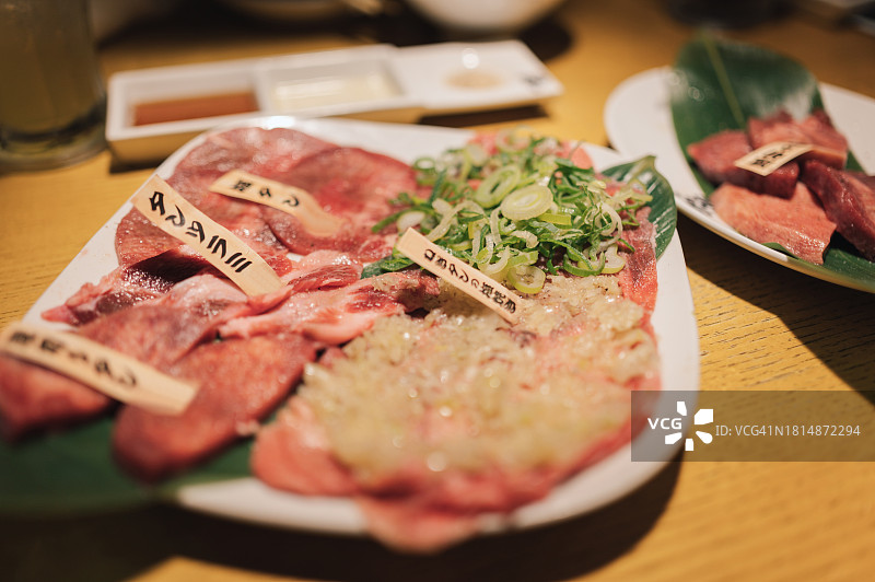 年轻亚洲女性在餐厅吃日式烤肉，将生牛肉片放在炭火烤炉上的特写图片素材