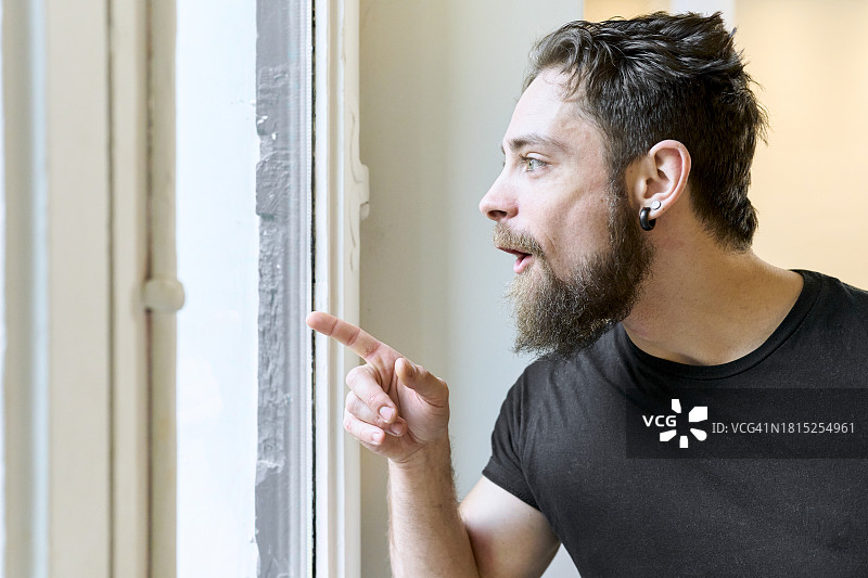 休闲装男子微笑指向公寓窗户的侧面图图片素材