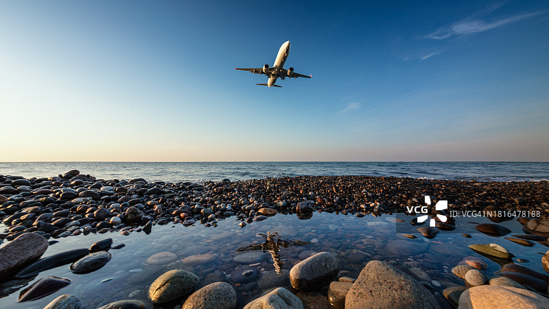 日落时分在卵石海滩上空降落的飞机图片素材