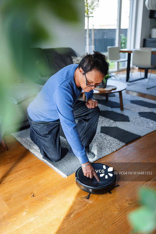 在现代住宅中使用机器人真空吸尘器的沉思老年男子图片素材