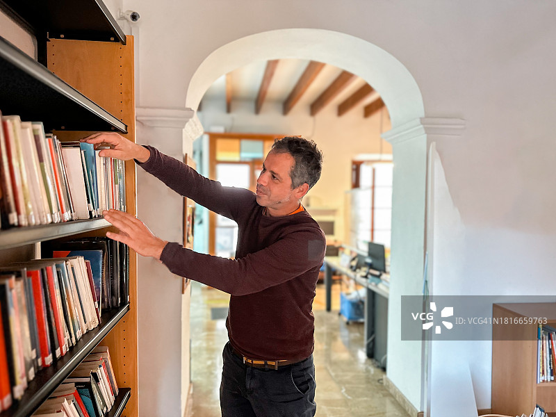 英俊的图书管理员在图书馆的书架上放书图片素材
