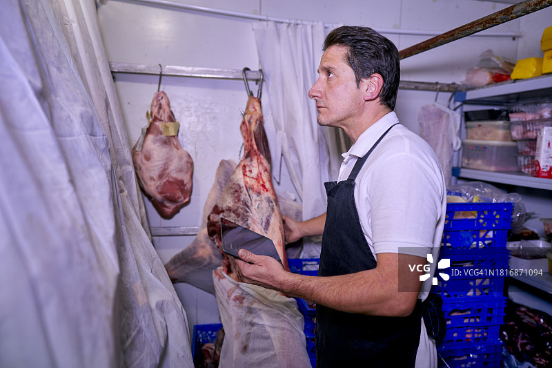 西班牙肉店的肉贩使用平板电脑管理库存和保质期图片素材