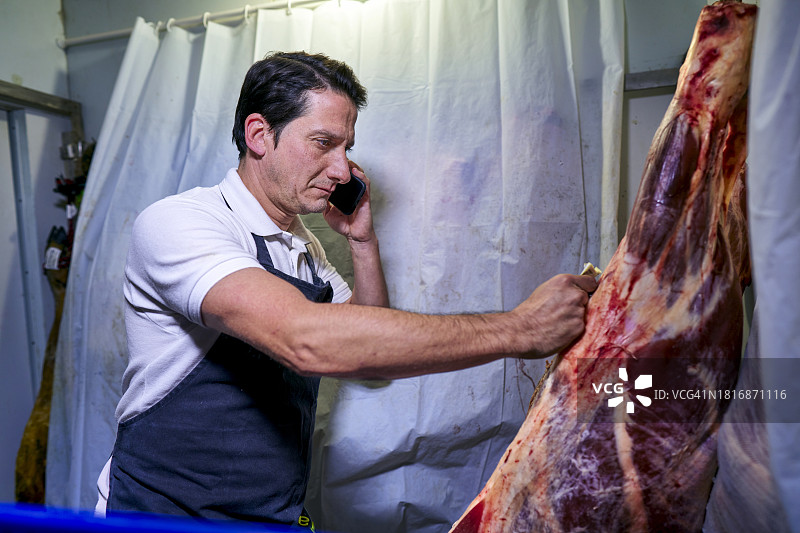 西班牙肉店店员检查冷藏室的肉品库存并致电经销商订货图片素材