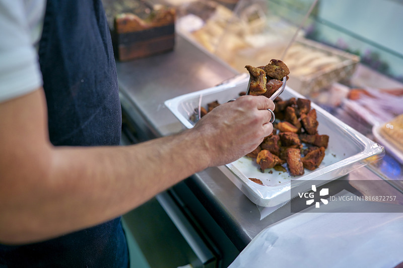 社区肉店里，西班牙肉贩为顾客挑选特色油渣图片素材
