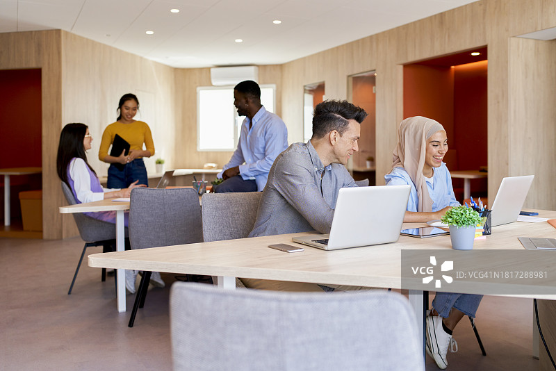在大型办公室工作的五位不同种族的人，大家在办公桌前微笑图片素材