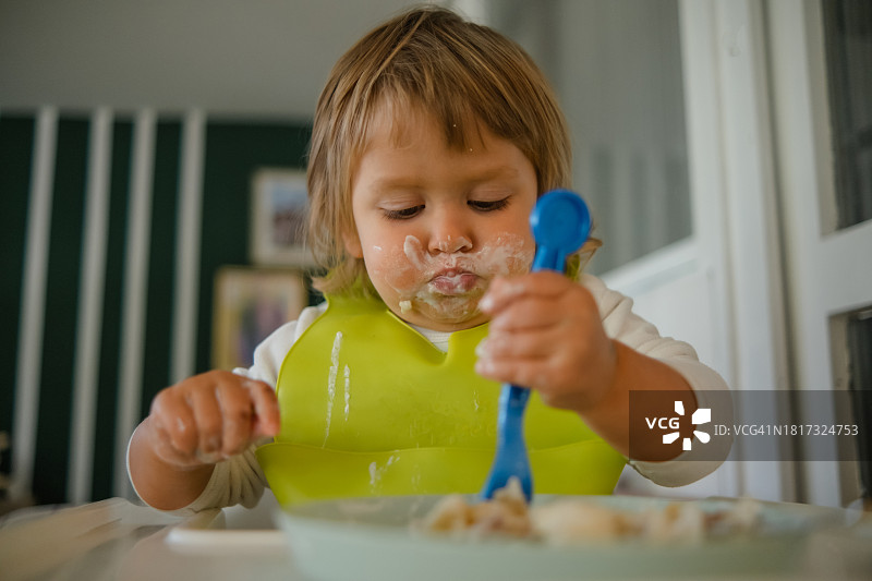 可爱的金发周岁女童用勺子吃饭图片素材