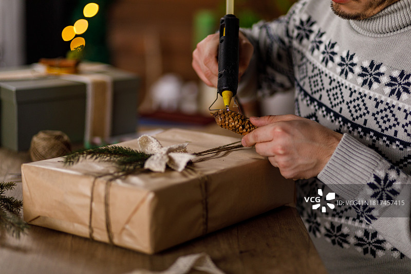 年轻男人用热熔胶枪在圣诞礼盒上粘松果图片素材