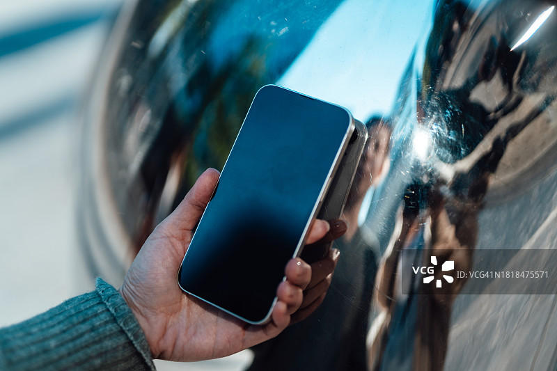女性手持智能手机特写（反射金属背景）图片素材