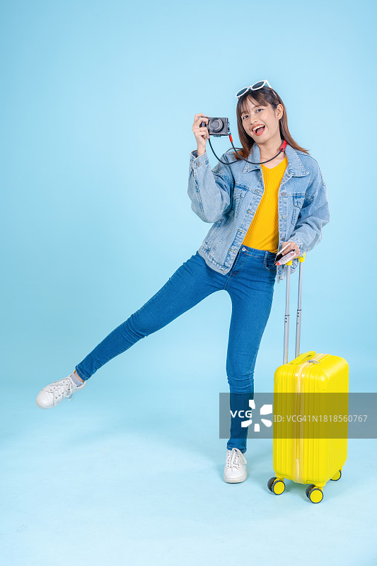 快乐的亚洲女性拖着行李箱在浅蓝色背景上行走，准备开启夏季旅行。图片素材