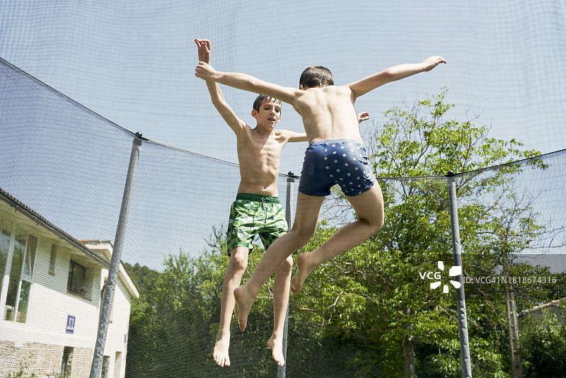晴天，花园里，穿泳衣的湿孩子们在蹦床上跳跃（后视图）图片素材