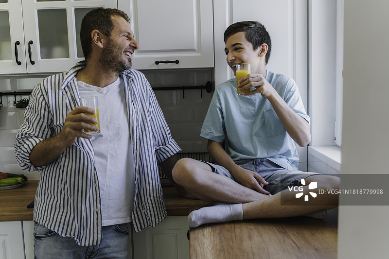 父亲在厨房喝果汁时和十几岁的儿子说话图片素材