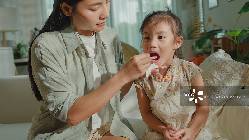 妈妈在家照顾发烧感冒的女儿，给孩子喂药，呵护生病的孩子，关注家庭健康图片素材