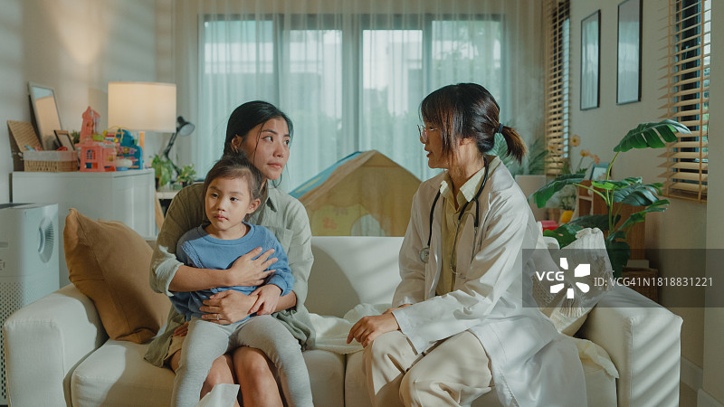 女医生在家中为发烧生病的女孩检查并提供建议，关注患病女孩与母亲的家庭健康图片素材