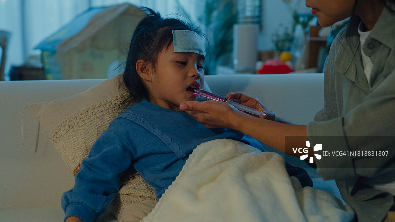 妈妈在家照顾发高烧生病的女儿，并在夜间用注射器喂药图片素材