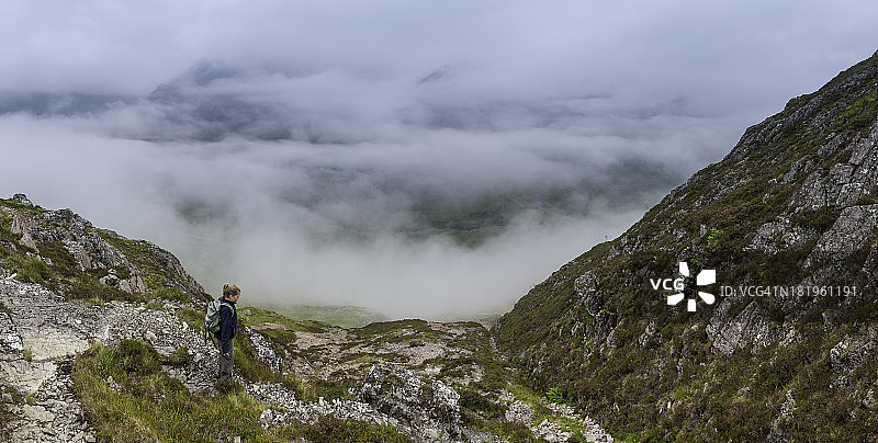 女孩徒步者在云层之上的山间小径图片素材